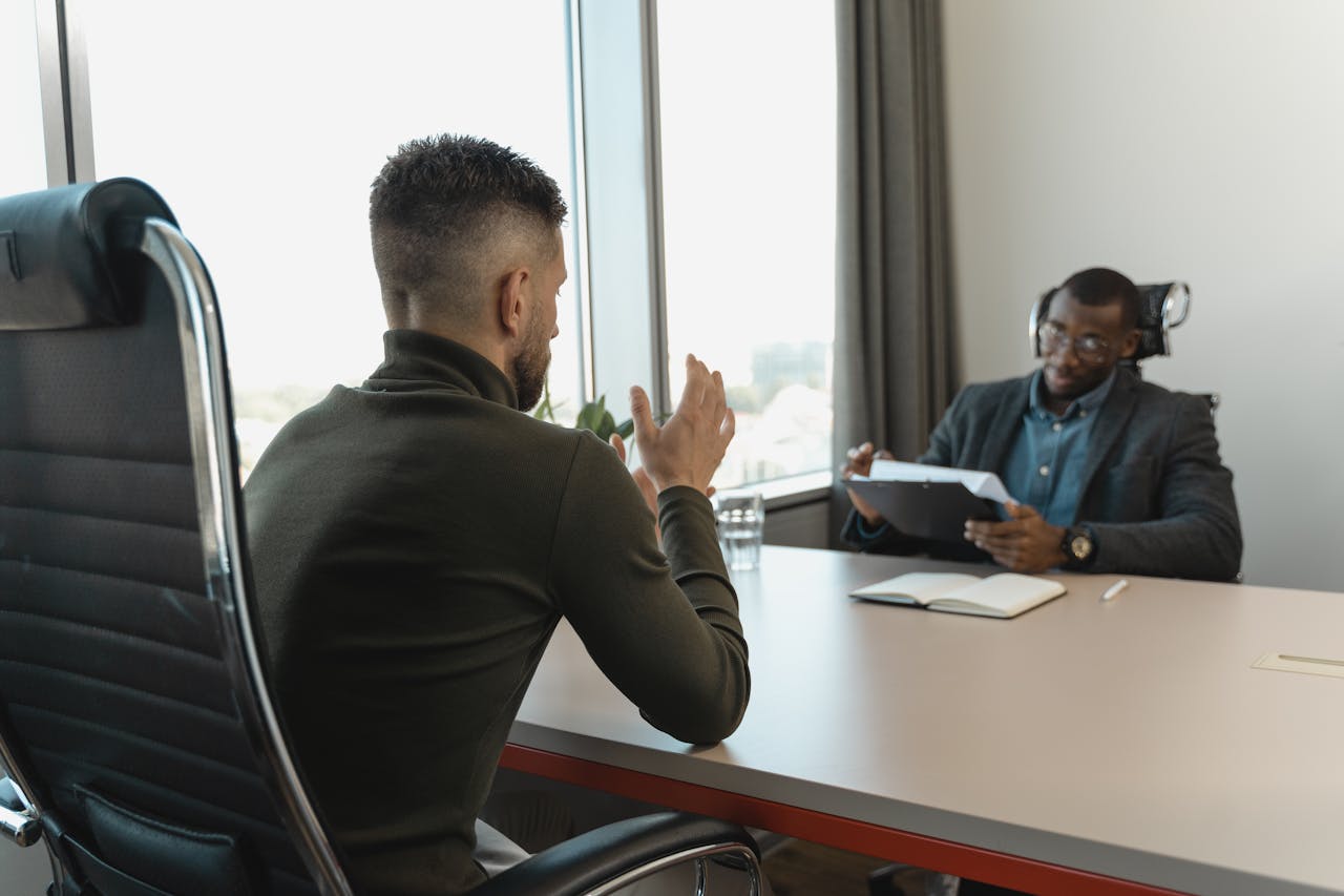 Two men in a job interview setting in a modern office with large windows.