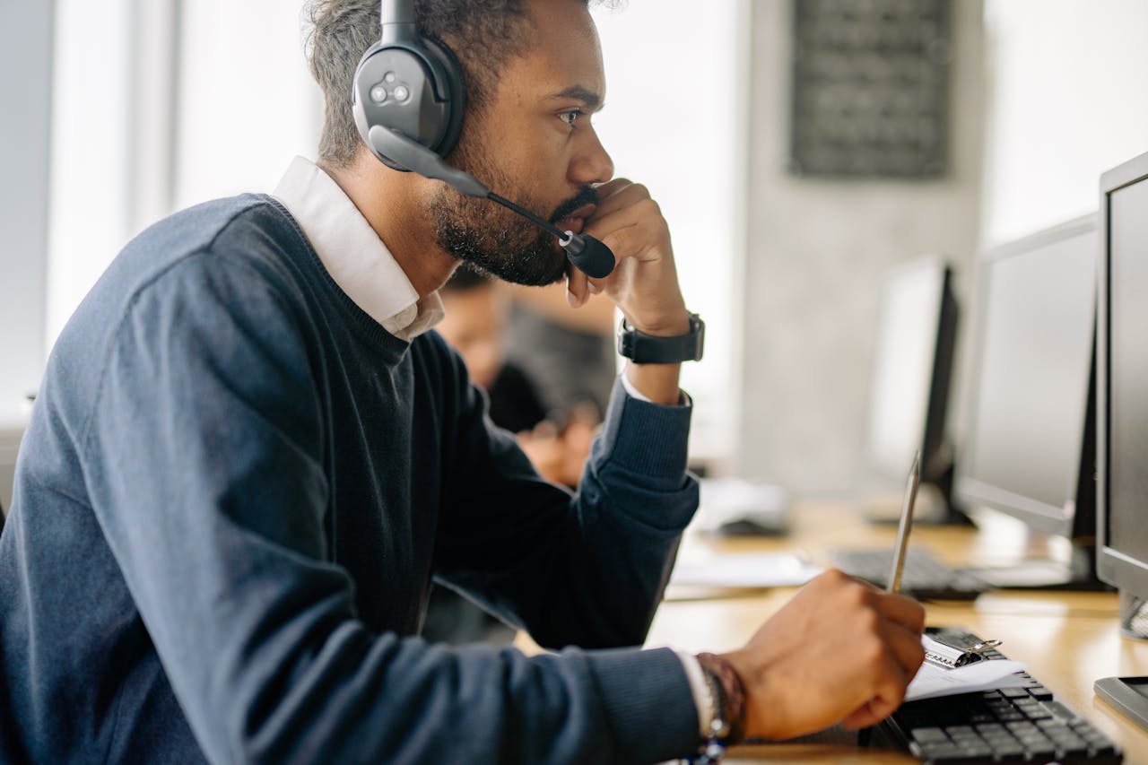 Side view of a bearded man in a headset concentrating at his desk in an office environment.