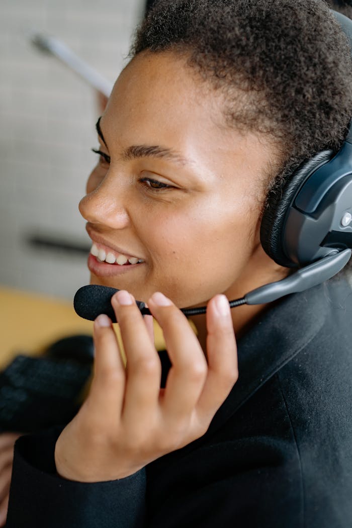 A smiling woman uses a headset while engaged in online communication, showing happiness and connectivity.