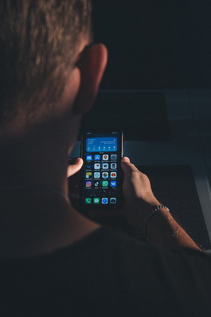 Close-up of a person holding a smartphone with apps visible on screen in a dimly lit environment.